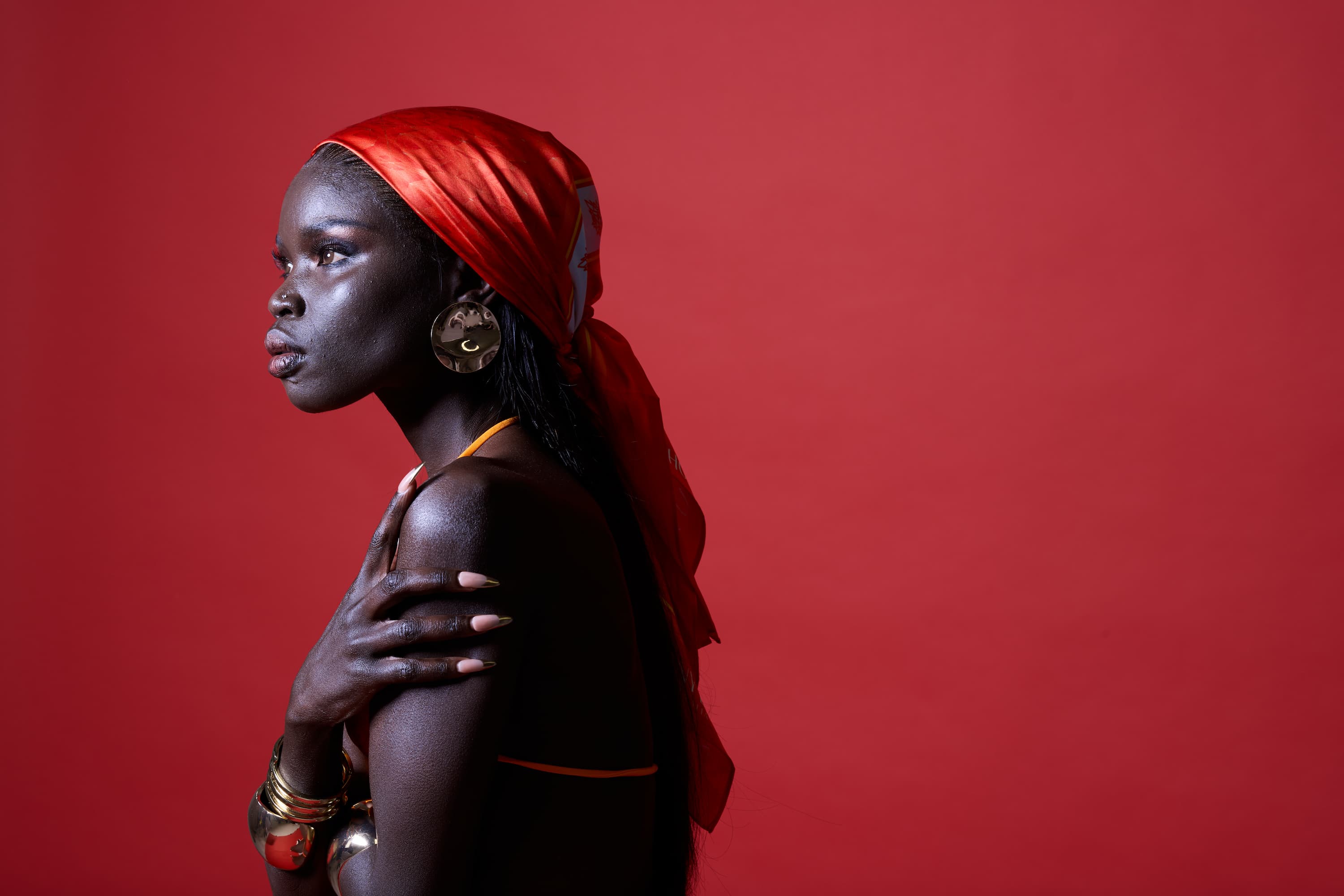 Woman with a red headscarf and gold jewelry against a red background
